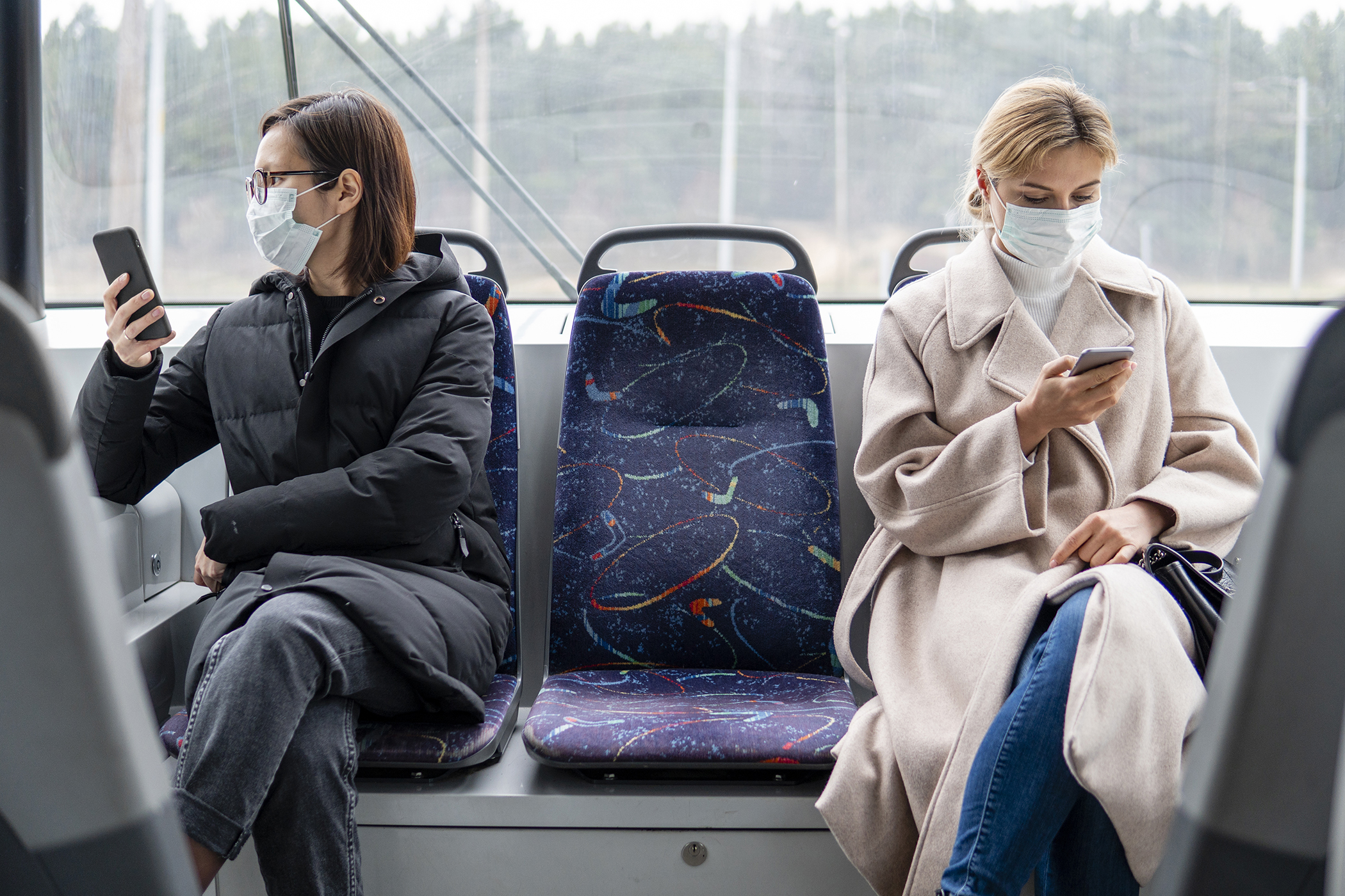 two people sitting on a bus with masks on on their phone